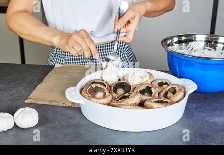 Una donna prepara un piatto di funghi ripieni al forno con erbe fresche in una cucina moderna. Foto Stock