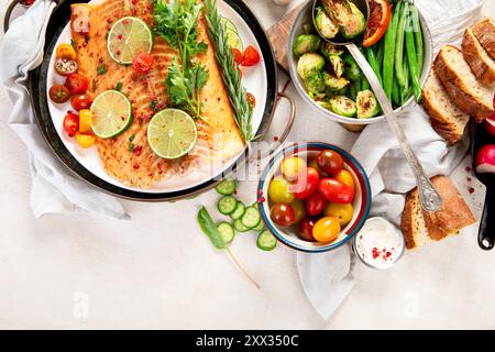 Salmone e verdure alla griglia su sfondo chiaro in legno. Tavolo da pranzo con pesce cotto, pomodori, asparagi. Vista dall'alto Foto Stock