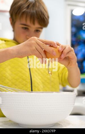 Bambino che apre un uovo in un recipiente per cuocere dei biscotti Foto Stock