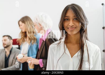 Ritratto di una giovane donna d'affari a colori in un ambiente d'ufficio diversificato. L'immagine mostra l'inclusione sul luogo di lavoro, il lavoro di squadra multiculturale e la tecnologia fem Foto Stock