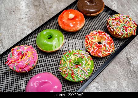Un vassoio di mini ciambelle colorate con spruzzi sulla parte superiore. Le mini ciambelle sono disposte in fila, alcune sono verdi e altre rosa. Il vassoio è Foto Stock