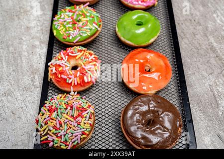 Un vassoio di mini ciambelle colorate con spruzzi sulla parte superiore. Le mini ciambelle sono disposte in fila, alcune sono verdi e altre rosa. Il vassoio è Foto Stock