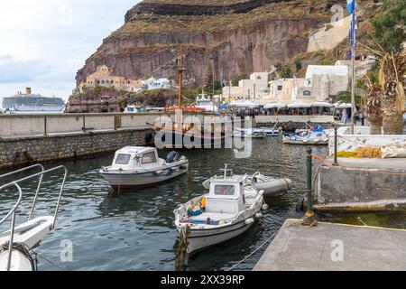 Santorini, Grecia - 8 ottobre 2019: Sereno porto con barche ormeggiate contro scogliere torreggianti. Foto Stock