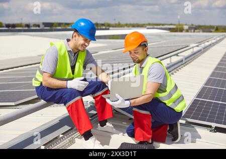 Tecnici dei pannelli solari che eseguono l'installazione o la manutenzione utilizzando un computer portatile Foto Stock