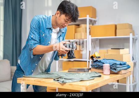 Giovane venditore online che scatta foto del suo prodotto per camicia da utilizzare sul suo sito Web e recensione online presso il suo studio di casa Foto Stock