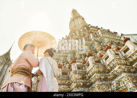 Bangkok, Thailandia - 11 febbraio 2024: Giovani coppie thailandesi indossano abiti tradizionali per una sessione fotografica al Wat Arun bellissimo tempio buddista sul sole caldo Foto Stock