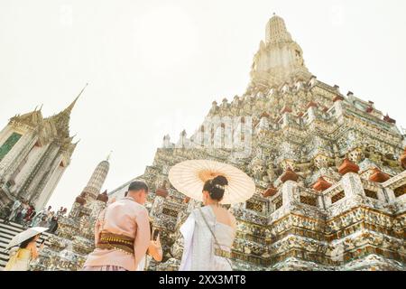 Bangkok, Thailandia - 11 febbraio 2024: Giovani coppie thailandesi indossano abiti tradizionali per una sessione fotografica al Wat Arun bellissimo tempio buddista sul sole caldo Foto Stock