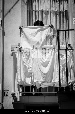 Una donna esce dal bucato sul balcone di casa sua Foto Stock