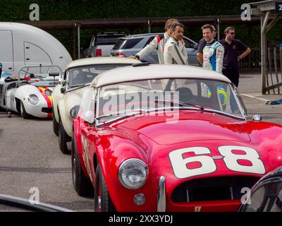 Una linea di auto da corsa e piloti tra cui Dario Franchitti nel paddock in occasione di una giornata di prova Goodwood Revival 2024 Foto Stock