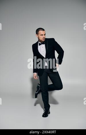 Uomo in smoking nero, cravatta, guarda con fiducia lontano con la gamba incrociata. Foto Stock