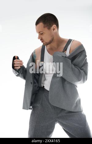 Un uomo vestito elegantemente si posa in un ambiente da studio, indossando una tuta grigia e una canotta bianca. Foto Stock