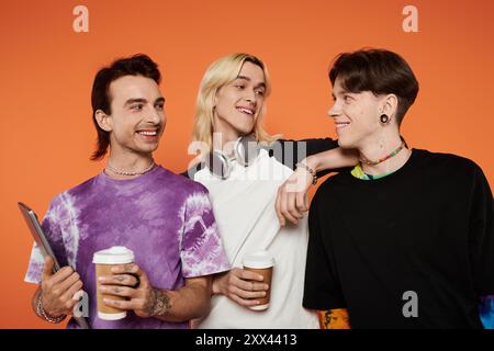 Tre giovani amici che indossano abiti vivaci si mettono insieme su uno sfondo arancione. Foto Stock