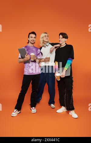 Tre giovani amici queer si posano insieme con un caffè su un vivace sfondo arancione. Foto Stock