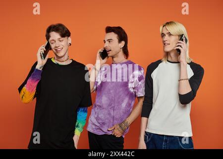 Tre giovani amici, vestiti con abiti eleganti e vivaci, si mettono in posa su uno sfondo arancione brillante mentre parlano al telefono. Foto Stock