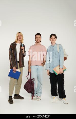 Tre giovani, vestiti in modo informale, stanno insieme di fronte a uno sfondo grigio. Foto Stock