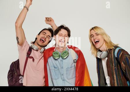 Tre giovani studenti, vestiti casualmente, posano con una bandiera arcobaleno e sorrisi, celebrando la loro amicizia e inclusività. Foto Stock