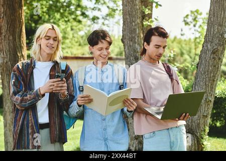 Tre amici LGBTQIA in abiti casual si godono una giornata di sole all'aperto: Uno legge, l'altro usa un telefono e il terzo lavora su un notebook. Foto Stock