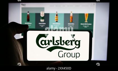 Persona che possiede uno smartphone con il logo dell'azienda danese Carlsberg, COME davanti al sito Web. Mettere a fuoco il display del telefono. Foto Stock