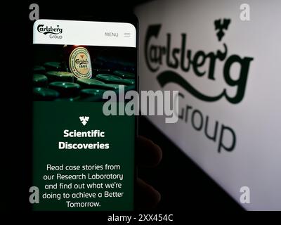 Persona che detiene lo smartphone con pagina Web della birreria danese Carlsberg COME davanti al logo aziendale. Messa a fuoco al centro del display del telefono. Foto Stock