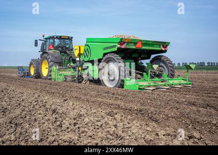 Un agricoltore che utilizza un trattore e un attrezzo di piantagione, pianta patate nei fertili campi agricoli dei Paesi Bassi. Foto Stock