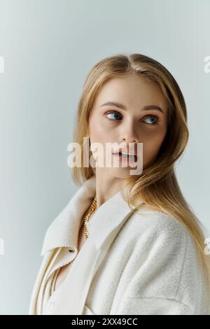 Una giovane donna dai lunghi capelli biondi, vestita con un cappotto bianco, guarda lontano. Foto Stock