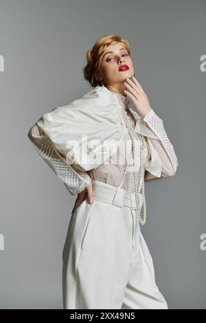Una giovane donna con una blusa bianca rifinita in pizzo e pantaloni coordinati si posa su uno sfondo grigio. Foto Stock