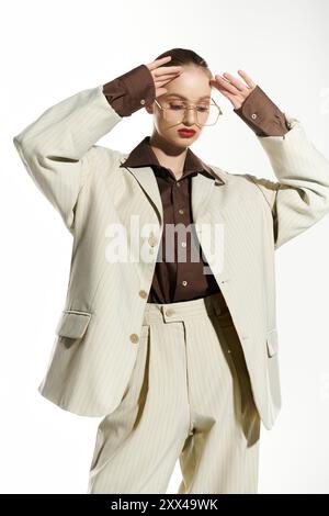 Una donna posa indossando un abito beige, una camicia marrone e occhiali dorati. Foto Stock