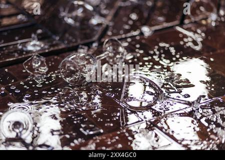 Primo piano di bicchieri da vino rotti e di vino versato, parti del bicchiere rotto sul pavimento con acqua spruzzata, Foto Stock