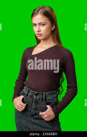 Giovane donna che posa con il maglione Borgogna e i jeans contro lo schermo verde Foto Stock