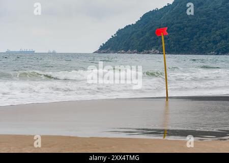 Un cartello rosso bloccato nella sabbia sulla spiaggia indica una zona pericolosa del mare, in modo che i nuotatori non entrino in questa zona. Foto Stock
