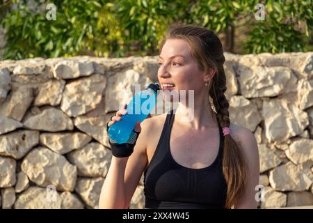 Un giovane con i capelli di rame pratica yoga e Pilates in natura, gustando una bevanda energetica in una giornata di sole. Foto Stock