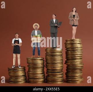 Persone di varie professioni su pile di monete di diversa altezza su sfondo marrone Foto Stock