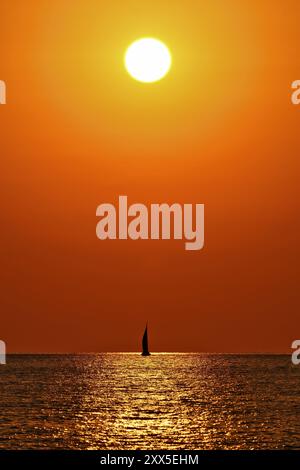 Tramonto sul mare con la silhouette di una barca a vela all'orizzonte Foto Stock