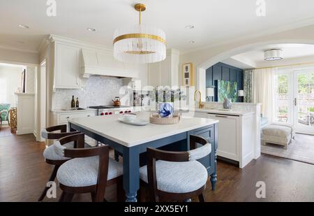 Vista ad angolo della cucina bianca con isola blu e vista sulla sala TV con ingresso ad arco Foto Stock
