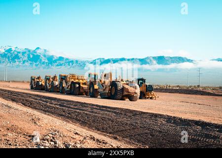 Una flotta di traslocatori di terra prepara terreni desertici aridi per lo sviluppo di nuove abitazioni. Le montagne si insinuano sullo sfondo mentre le attrezzature da costruzione si trasformano Foto Stock