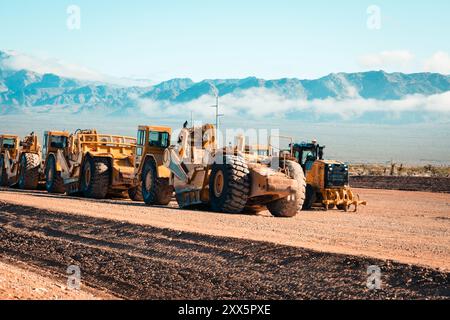 Una flotta di traslocatori di terra prepara terreni desertici aridi per lo sviluppo di nuove abitazioni. Le montagne si insinuano sullo sfondo mentre le attrezzature da costruzione si trasformano Foto Stock