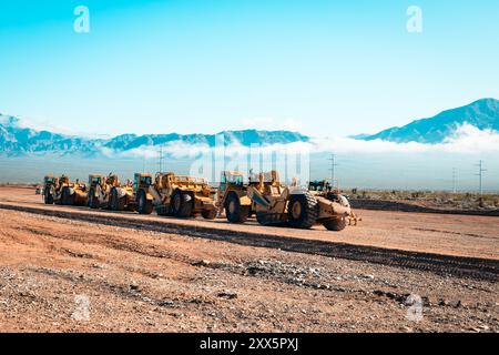 Una flotta di traslocatori di terra prepara terreni desertici aridi per lo sviluppo di nuove abitazioni. Le montagne si insinuano sullo sfondo mentre le attrezzature da costruzione si trasformano Foto Stock