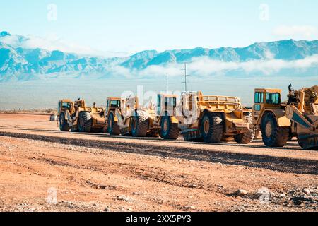 Una flotta di traslocatori di terra prepara terreni desertici aridi per lo sviluppo di nuove abitazioni. Le montagne si insinuano sullo sfondo mentre le attrezzature da costruzione si trasformano Foto Stock