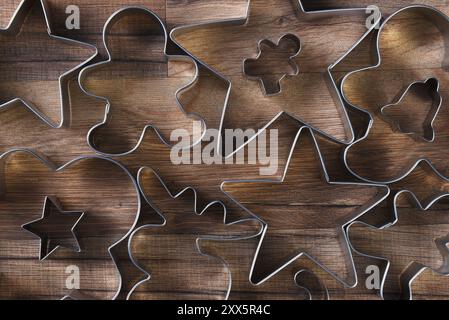 Primo piano vista dall'alto di un gruppo di taglierine per biscotti assortite di varie forme su un tavolo da cucina in legno. Stelle, uomini di pan di zenzero, alci, campana e caramelle CA Foto Stock