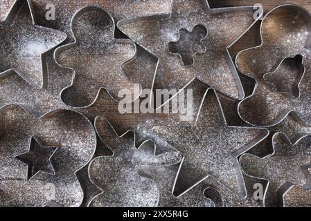 Vista dall'alto di un gruppo di fornelli assortiti di varie forme su un tavolo da cucina in legno cosparso di farina. Stelle, uomini di pan di zenzero, Mo Foto Stock