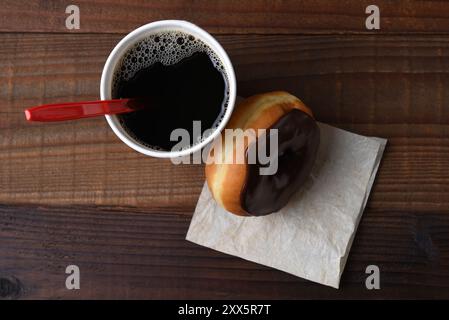 Colpo ad angolo alto di ciambella smerigliata al cioccolato appoggiata su una tazza calda di caffè appena estratto. Foto Stock