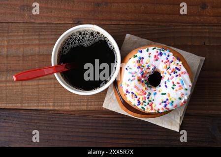 Vista ad angolo alto di una tazza di carta di caffè caldo appena preparato accanto a una pila di ciambelle. Foto Stock