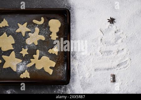 Concetto di cottura per le vacanze. Vista dall'alto di una teglia da forno e biscotti natalizi su un ripiano ricoperto di farina a forma di albero di Natale. Foto Stock