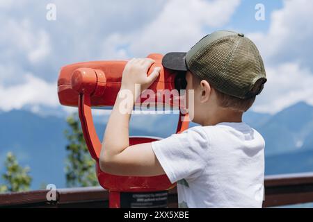 ragazzo che osserva il panorama delle montagne attraverso un binocolo fisso Foto Stock