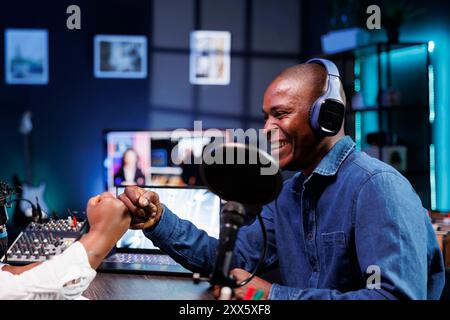 Il simpatico ospite maschile colpisce un individuo, dando il benvenuto all'ospite nel suo talk show online. Allegri influencer si salutano a vicenda, si preparano a trasmettere un episodio podcast dal vivo da casa. Foto Stock