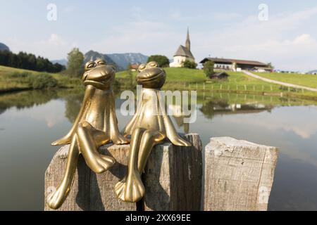 Due rane di ottone, dietro di loro la chiesa di San Nicola, Einsiedl, Inzell, Baviera, Germania, Europa Foto Stock