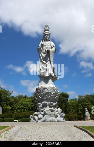 Grande statua in pietra di una figura maestosa di fronte a un cielo blu con nuvole, circondata da alberi verdi, Bacalhoa, Bacalhoa Buddha Eden, Quinta dos Lor Foto Stock