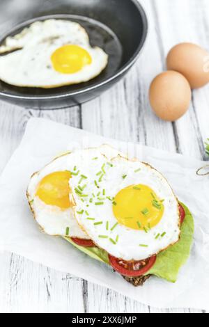 Panino con uova fritte appena sfornate (primo piano dettagliato, messa a fuoco selettiva) su un tavolo di legno Foto Stock