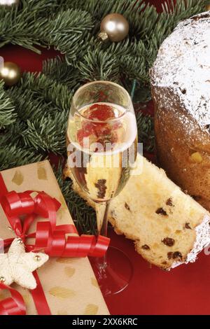 Panettone la torta alla frutta di Natale italiana, un bicchiere di spumante (champagne) e un regalo di Natale sotto l'albero di Natale, su sfondo rosso. S Foto Stock