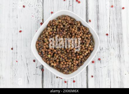 Grani di pepe rosa freschi (conservati) su un vecchio e rustico tavolo in legno, messa a fuoco selettiva, foto ravvicinata Foto Stock